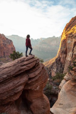 Bir uçurumun kenarında, maceracı kız güzel manzaralı Kanyon canlı bir gün batımı sırasında bakıyor. Zion National Park, Utah, Amerika Birleşik Devletleri'nde çekilen.