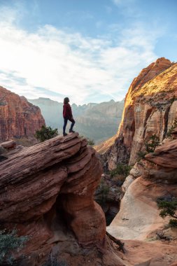Bir uçurumun kenarında, maceracı kız güzel manzaralı Kanyon canlı bir gün batımı sırasında bakıyor. Zion National Park, Utah, Amerika Birleşik Devletleri'nde çekilen.
