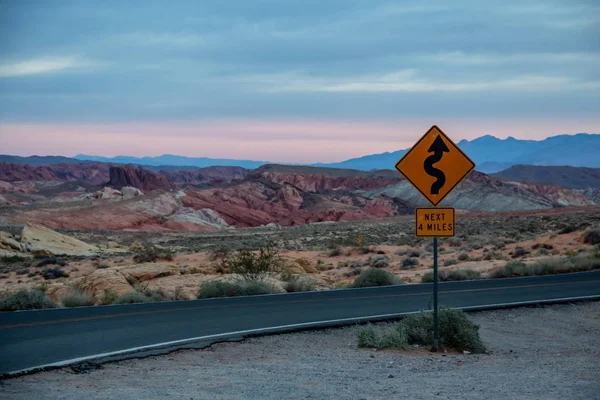 Winding road sign on a scenic road in the desert during a cloudy sunrise. Taken in Valley of Fire State Park, Nevada, United States.