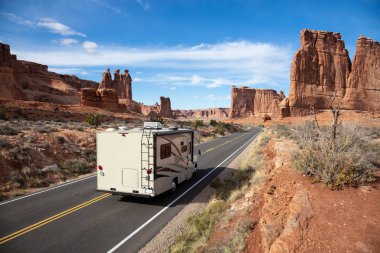 Camper riding on a Scenic road in the red rock canyons during a vibrant sunny day. Taken in Arches National Park, located near Moab, Utah, United States. clipart