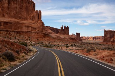 Landscape view of a Scenic road in the red rock canyons during a vibrant sunny day. Taken in Arches National Park, located near Moab, Utah, United States. clipart