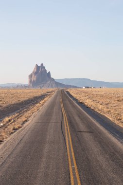 Shiprock dağ tepe canlı güneşli gün doğumu sırasında arka planda olan bir kuru çölde yol görünümünü. Çıngıraklı yılan, New Mexico, Amerika Birleşik Devletleri, alınan.