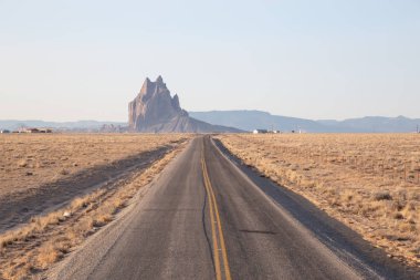 Shiprock dağ tepe canlı güneşli gün doğumu sırasında arka planda olan bir kuru çölde yol görünümünü. Çıngıraklı yılan, New Mexico, Amerika Birleşik Devletleri, alınan.
