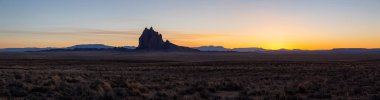 Striking panoramic landscape view of a dry desert with a mountain peak in the background during a vibrant sunset. Taken at Shiprock, New Mexico, United States. clipart