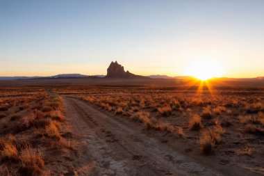 Manzaralı bir dağ tepe ile Kuru çölde bir toprak yol, canlı bir gün batımı sırasında arka planda dikkat çekici. Shiprock, New Mexico, Amerika Birleşik Devletleri, alınan.