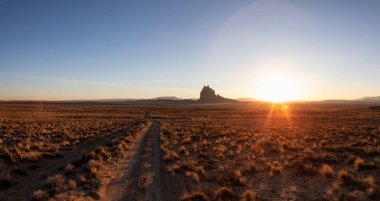 Bir dağ tepe ile Kuru çölde bir toprak yol görünümünü panoramik manzara canlı bir gün batımı sırasında arka planda dikkat çekici. Shiprock, New Mexico, Amerika Birleşik Devletleri, alınan.
