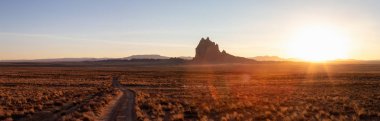 Bir dağ tepe ile Kuru çölde bir toprak yol görünümünü panoramik manzara canlı bir gün batımı sırasında arka planda dikkat çekici. Shiprock, New Mexico, Amerika Birleşik Devletleri, alınan.