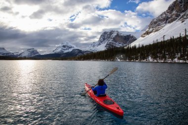 Bir bulutlu sabah sırasında Kanada Rocky Dağları ile çevrili bir buzul Gölü'kayak maceracı kız. Alınan yay Gölü, Banff, İngiltere.