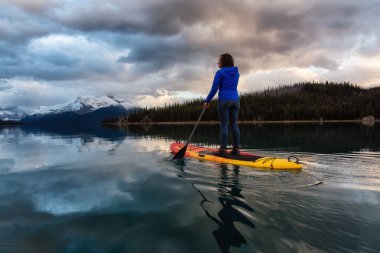 Kız yatılı raket huzurlu ve sakin buzul Göl canlı bir bulutlu gün batımı sırasında. Maligne gölde, Jasper National Park, Alberta, Kanada alınan.
