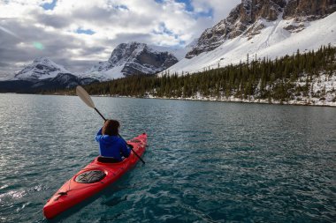 Bir bulutlu sabah sırasında Kanada Rocky Dağları ile çevrili bir buzul Gölü'kayak maceracı kız. Alınan yay Gölü, Banff, İngiltere.