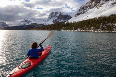 Bir bulutlu sabah sırasında Kanada Rocky Dağları ile çevrili bir buzul Gölü'kayak maceracı kız. Alınan yay Gölü, Banff, İngiltere.
