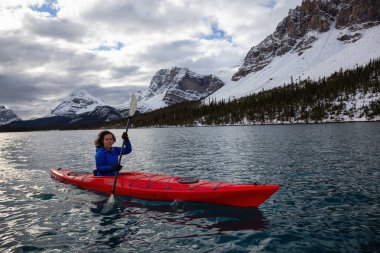 Bir bulutlu sabah sırasında Kanada Rocky Dağları ile çevrili bir buzul Gölü'kayak maceracı kız. Alınan yay Gölü, Banff, İngiltere.