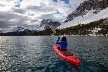 Bir bulutlu sabah sırasında Kanada Rocky Dağları ile çevrili bir buzul Gölü'kayak maceracı kız. Alınan yay Gölü, Banff, İngiltere.