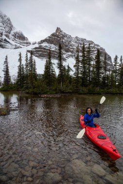Bir bulutlu sabah sırasında Kanada Rocky Dağları ile çevrili bir buzul Gölü'kayak maceracı kız. Alınan yay Gölü, Banff, İngiltere.