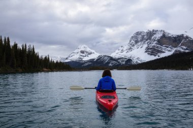 Bir bulutlu sabah sırasında Kanada Rocky Dağları ile çevrili bir buzul Gölü'kayak maceracı kız. Alınan yay Gölü, Banff, İngiltere.