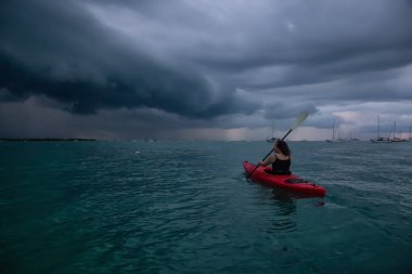 Kırmızı kayık maceracı kız doğru bir fırtına sırasında dramatik bir gün batımı kayak. Key West, Florida Keys, Amerika Birleşik Devletleri alınan.