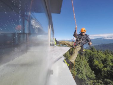 High Rise Rope Technician is hangining on the side of the building and power washing. Taken in Burnaby, Vancouver, BC, Canada.