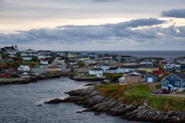Bir bulutlu gün batımı sırasında kayalık Atlantik Okyanusu kıyısında küçük bir kasaba evlerinde. Kanal-Port aux Bask, alınan Newfoundland, Canada.