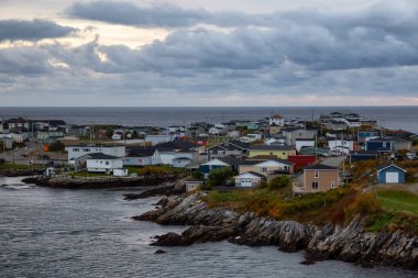 Bir bulutlu gün batımı sırasında kayalık Atlantik Okyanusu kıyısında küçük bir kasaba evlerinde. Kanal-Port aux Bask, alınan Newfoundland, Canada.