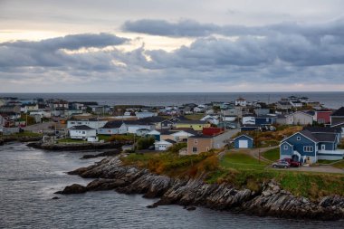 Bir bulutlu gün batımı sırasında kayalık Atlantik Okyanusu kıyısında küçük bir kasaba evlerinde. Kanal-Port aux Bask, alınan Newfoundland, Canada.