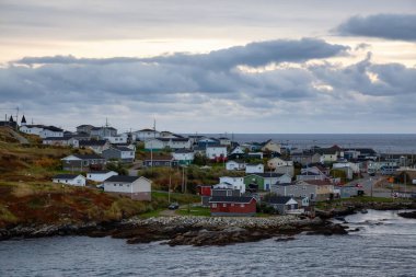 Bir bulutlu gün batımı sırasında kayalık Atlantik Okyanusu kıyısında küçük bir kasaba evlerinde. Kanal-Port aux Bask, alınan Newfoundland, Canada.