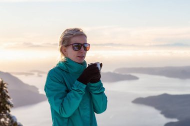 Genç beyaz kız sıcak içecek bir dağın tepesinde bir güzel kış günbatımı sırasında içme. Mnt Harvey, Vancouver, Bc, Kanada yakın üzerinde gerçekleştirilen.