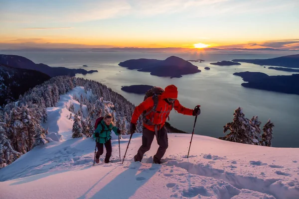 Adventure seeking man and woman are hiking to the top of a mountain during a vibrant winter sunset. Taken in Mnt Harvey, North of Vancouver, BC, Canada.