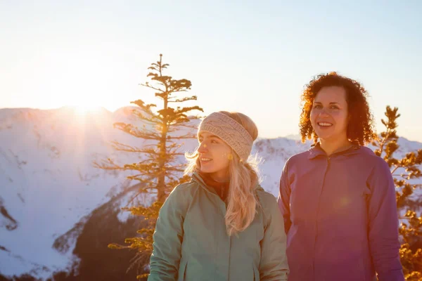 Couple friends are socializing on top of a mountain during a vibrant winter sunset. Taken on top of Zoa Peak near Hope, British Columbia, Canada.