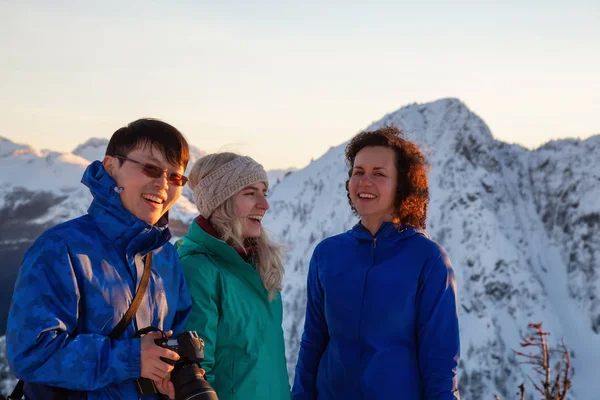 Group of friends are socializing on top of a mountain during a vibrant winter sunset. Taken on top of Zoa Peak near Hope, British Columbia, Canada.