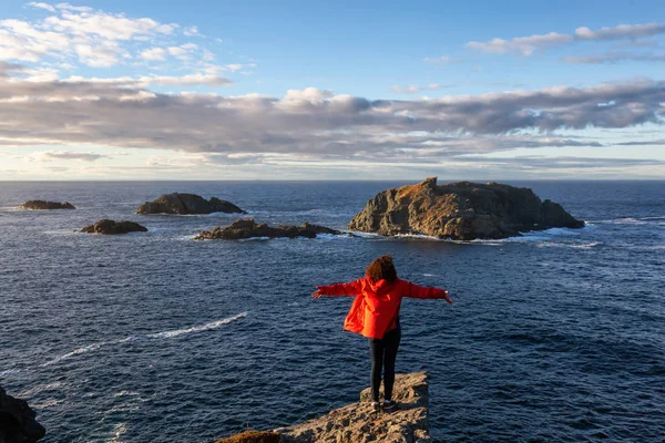身穿红色夹克的妇女张开双臂站在悬崖边 欣赏美丽的海洋风光 拍摄于加拿大纽芬兰和拉布拉多北双线岛的 Head — 图库照片