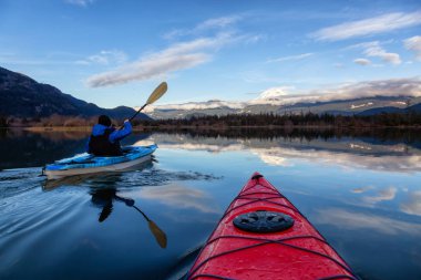 Adventurous man kayaking in peaceful water during a cloudy winter day. Taken in Squamish, North of Vancouver, BC, Canada. clipart