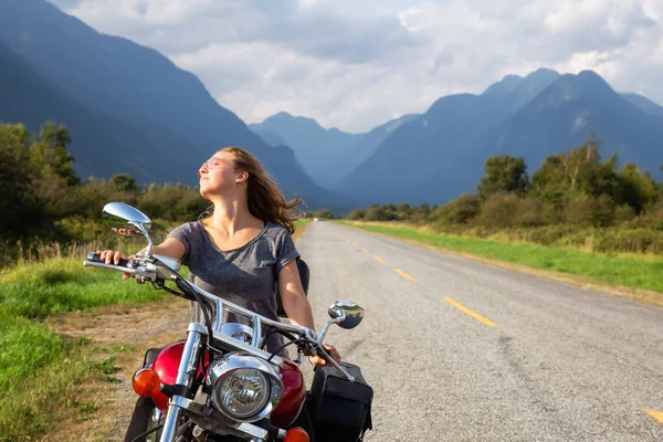 Woman riding a motorcycle on a scenic road surrounded by Canadian Mountains. Taken in Pitt Meadows, Greater Vancouver, BC, Canada.