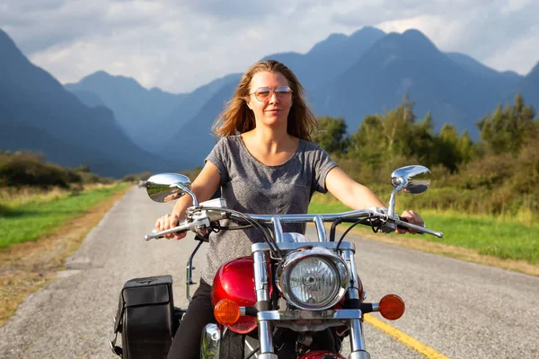 Woman riding a motorcycle on a scenic road surrounded by Canadian Mountains. Taken in Pitt Meadows, Greater Vancouver, BC, Canada.