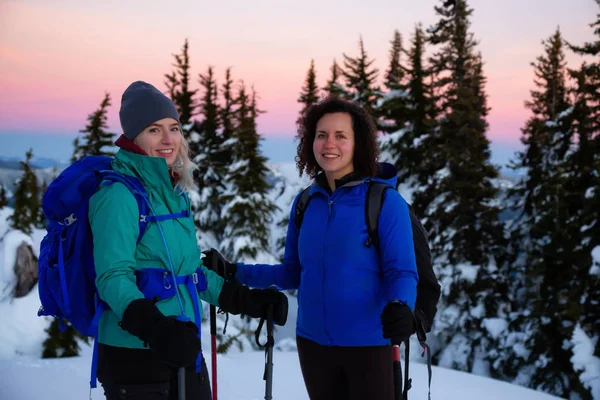 Couple friends are socializing on top of a mountain during a vibrant winter sunset. Taken on top of Zoa Peak near Hope, British Columbia, Canada.