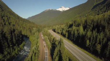 Güneşli bir yaz günü boyunca Güzel Kanada Dağları ile çevrili doğal bir yol yakınında bir trenhavadan görünümü. Revelstoke, British Columbia, Kanada yakınlarında çekilmiş.