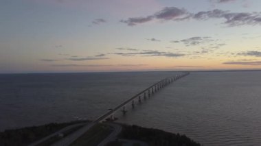Canlı bir gün batımı sırasında Cocagne Nehri üzerinden giden bir köprünün havadan görünümü. New Brunswick, Kanada'da çekilmiş.