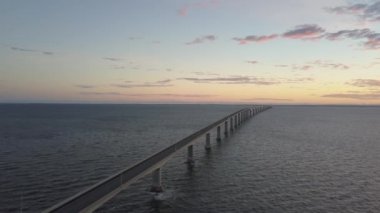 Canlı bir gün batımı sırasında Cocagne Nehri üzerinden giden bir köprünün havadan görünümü. New Brunswick, Kanada'da çekilmiş.