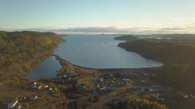 Aerial view of a small town on a rocky Atlantic Ocean Coast during a bright sunny sunrise. Taken in Little Bay, Newfoundland, Canada.