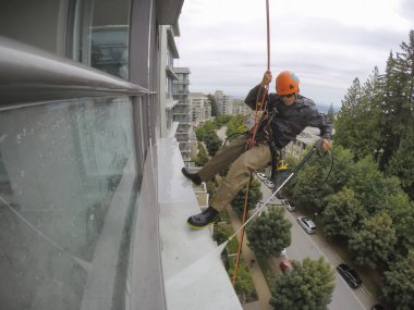 Burnaby, Vancouver, Bc, Kanada - 07 Temmuz 2018: Yüksek artış ip teknisyen hangining bina ve güç bir bulutlu gün boyunca yıkama tarafında olan.
