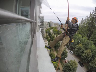 Burnaby, Vancouver, Bc, Kanada - 07 Temmuz 2018: Yüksek artış ip teknisyen hangining bina ve güç bir bulutlu gün boyunca yıkama tarafında olan.