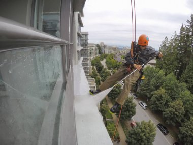 Burnaby, Vancouver, Bc, Kanada - 07 Temmuz 2018: Yüksek artış ip teknisyen hangining bina ve güç bir bulutlu gün boyunca yıkama tarafında olan.