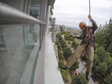 Burnaby, Vancouver, Bc, Kanada - 07 Temmuz 2018: Yüksek artış ip teknisyen hangining bina ve güç bir bulutlu gün boyunca yıkama tarafında olan.