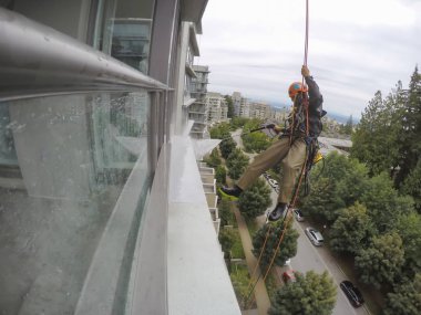 Burnaby, Vancouver, Bc, Kanada - 07 Temmuz 2018: Yüksek artış ip teknisyen hangining bina ve güç bir bulutlu gün boyunca yıkama tarafında olan.