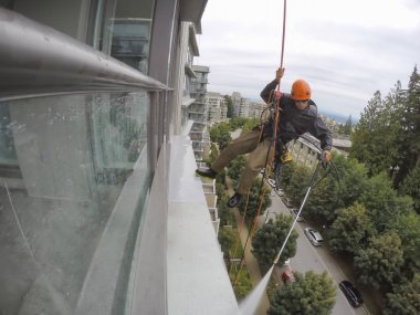 Burnaby, Vancouver, Bc, Kanada - 07 Temmuz 2018: Yüksek artış ip teknisyen hangining bina ve güç bir bulutlu gün boyunca yıkama tarafında olan.
