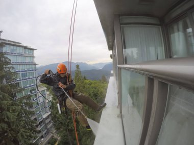 Burnaby, Vancouver, Bc, Kanada - 07 Temmuz 2018: Yüksek artış ip teknisyen hangining bina ve güç bir bulutlu gün boyunca yıkama tarafında olan.