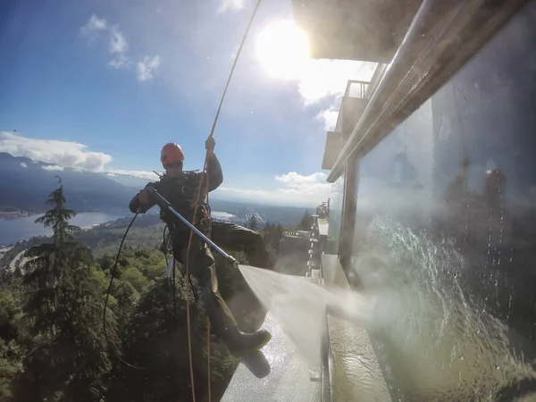 Burnaby, Vancouver, BC, Canada - July 08, 2018: High Rise Rope Technician is hangining on the side of the building and power washing.