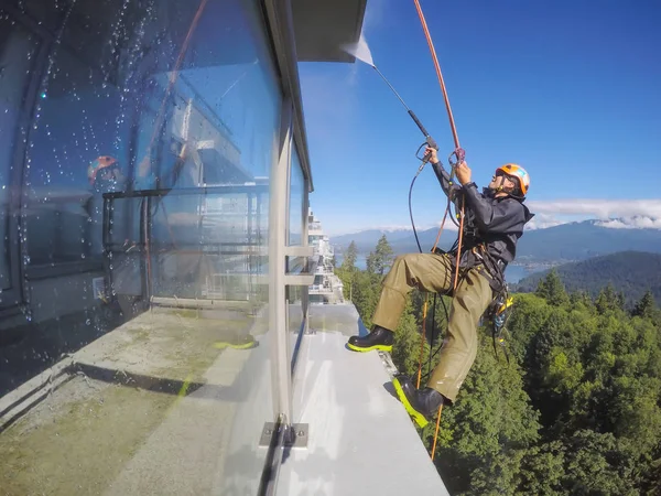 Burnaby, Vancouver, BC, Canada - July 08, 2018: High Rise Rope Technician is hangining on the side of the building and power washing.