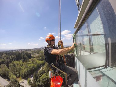 Burnaby, Vancouver, British Columbia, Kanada - 07 Temmuz 2018: Yüksek katlı halat erişim pencere temizleyici sıcak güneşli bir yaz günü boyunca çalışıyor.