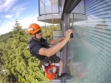 Burnaby, Vancouver, British Columbia, Kanada - 07 Temmuz 2018: Yüksek katlı halat erişim pencere temizleyici sıcak güneşli bir yaz günü boyunca çalışıyor.
