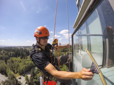 Burnaby, Vancouver, British Columbia, Kanada - 07 Temmuz 2018: Yüksek katlı halat erişim pencere temizleyici sıcak güneşli bir yaz günü boyunca çalışıyor.